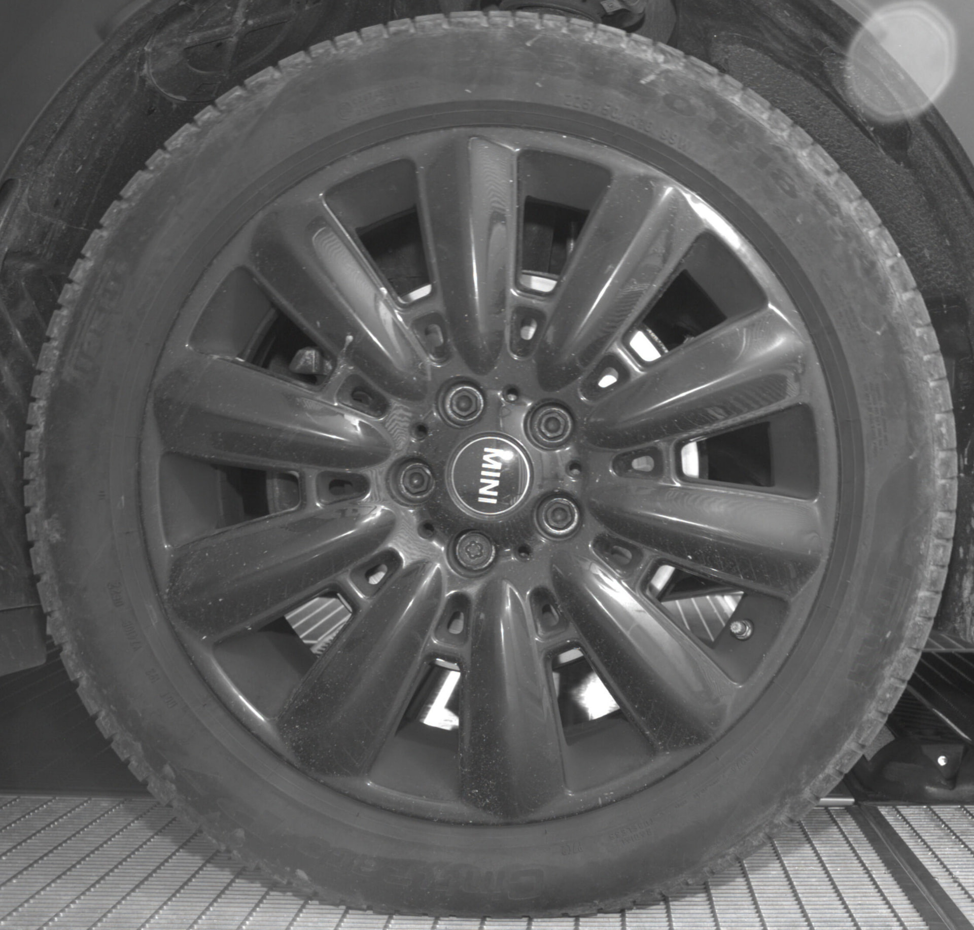 MINI alloy wheel photographed at a vehicle site entrance.