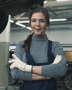 Smiling workshop receptionist welcoming a customer under a lifted vehicle.